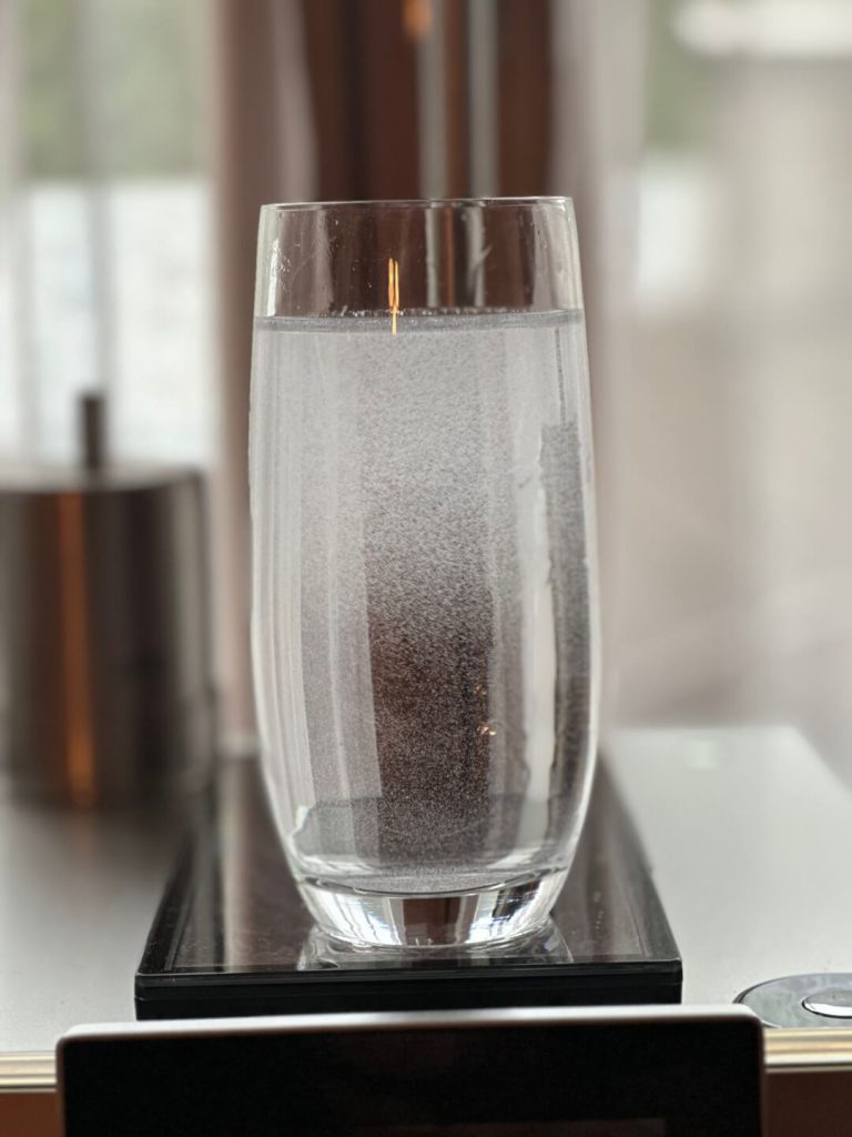 Milchig trübes Wasser im Glas auf einem Tisch, Hinweis auf mögliche Wasserqualität.
